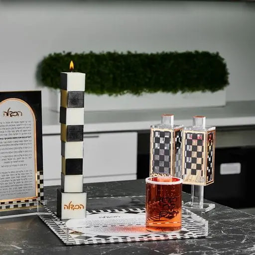 Onyx Havdalah Candle lit on a Havdalah table beside a spice holder, a checkered tray and a Havdalah card