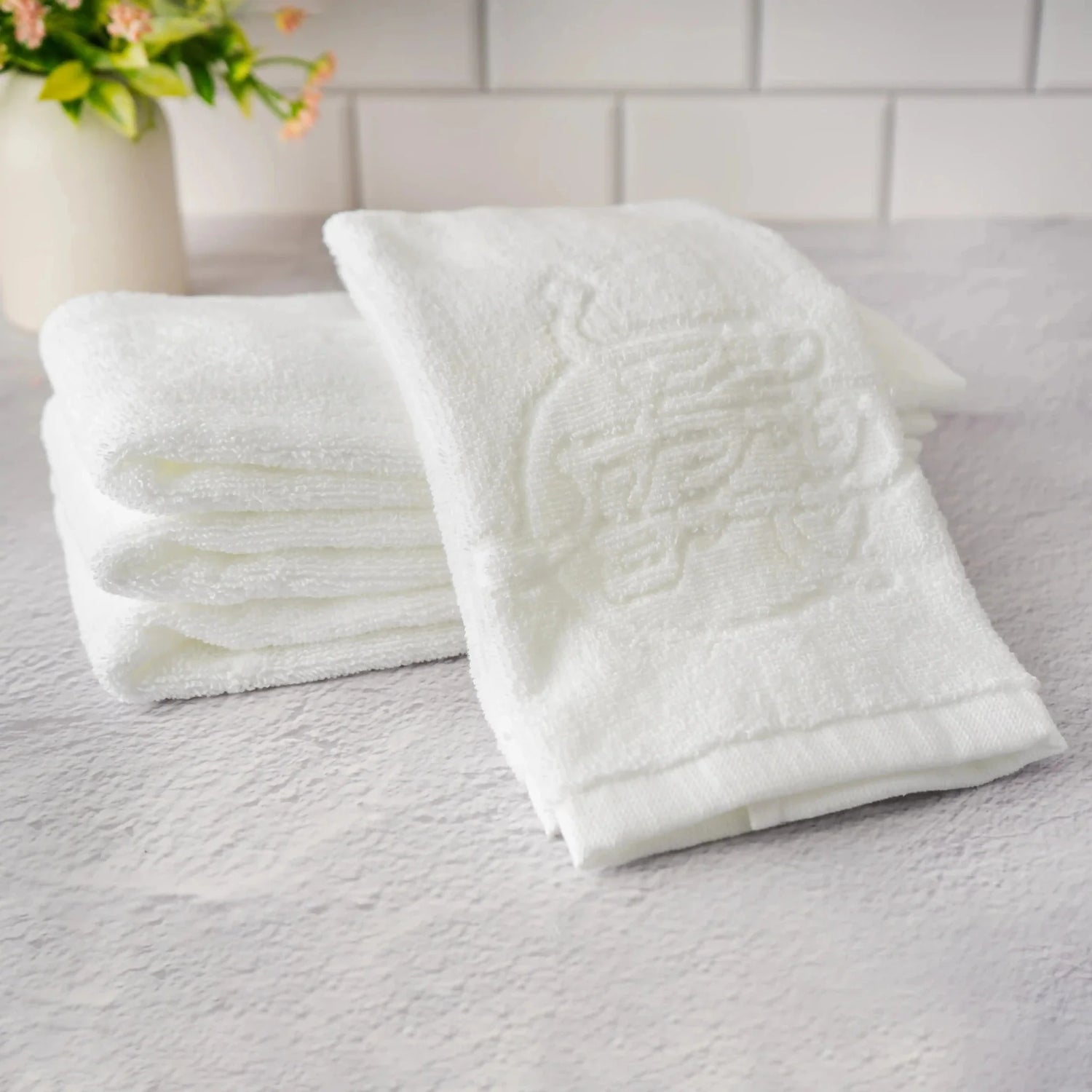 White Waterdale cotton hand towel with faint tone-on-tone wording, styled with folded towels